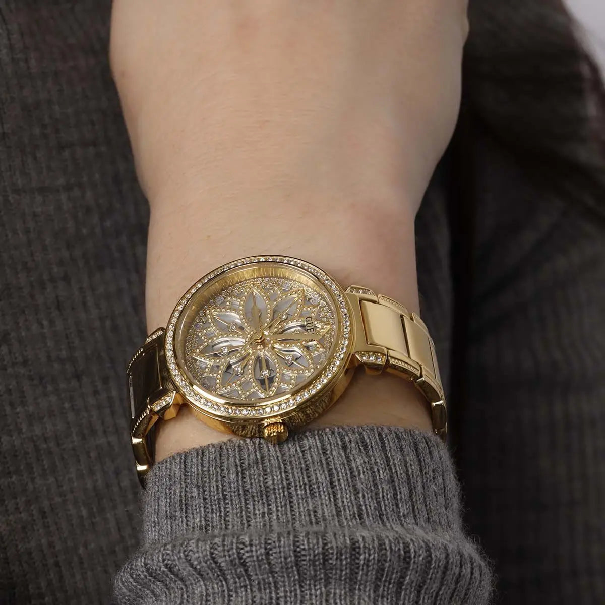 Guess Lily watch worn on wrist displaying floral crystal dial and gold bracelet detail